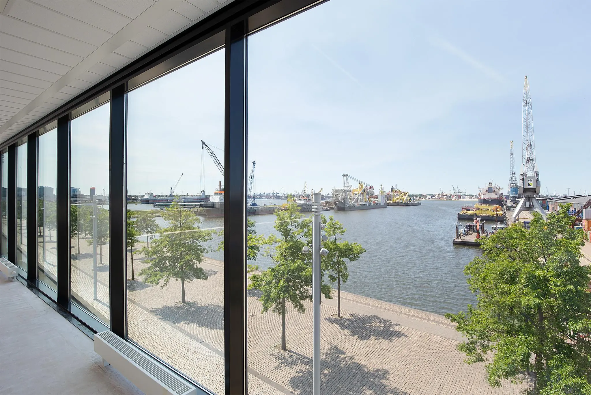 Uitzicht vanuit een modern kantoorgebouw op de Waalhaven Oostzijde met kranen, schepen en kade.